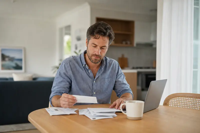 Man sorting through household bills at his dining table